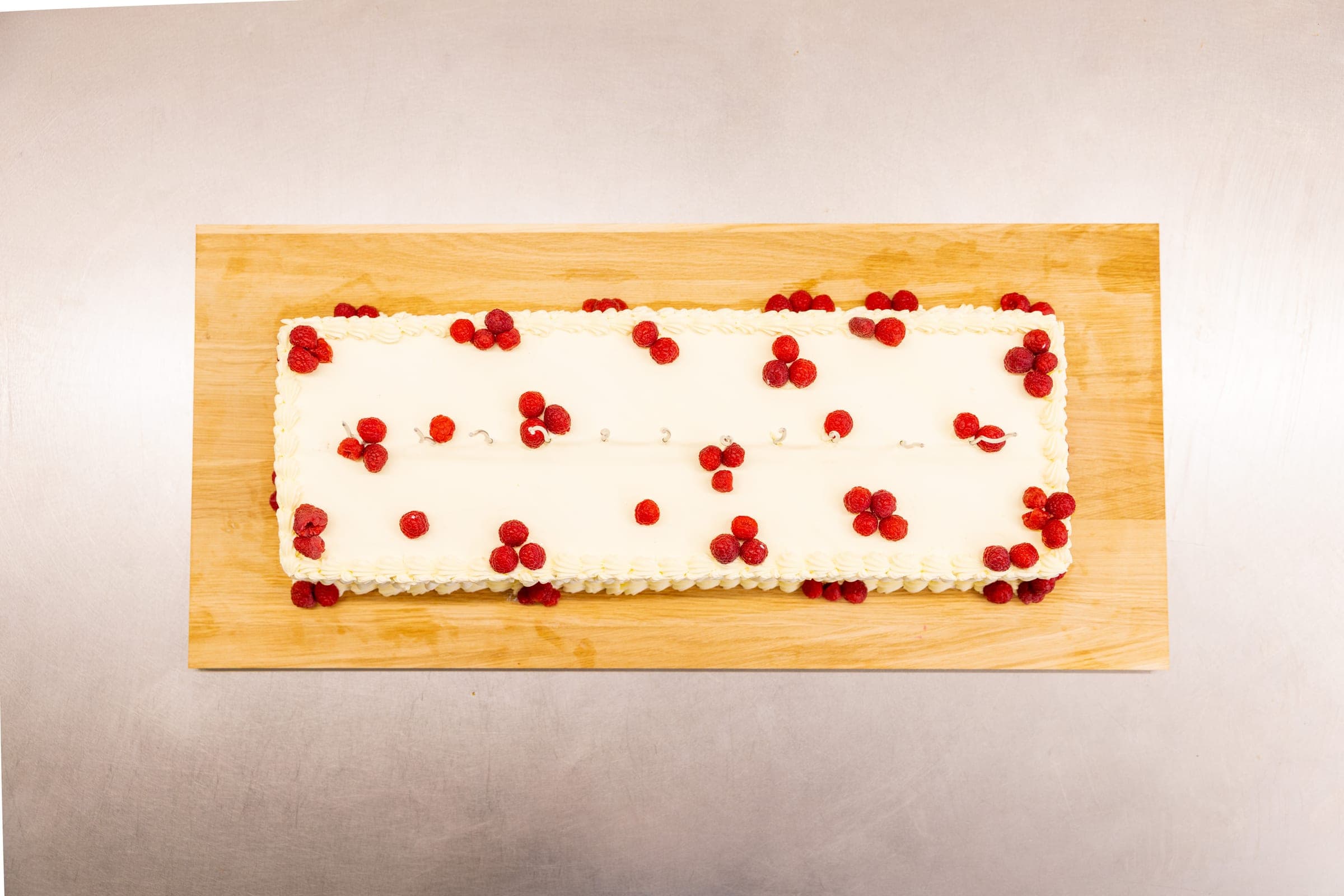 Lange rechteckige Sahneschnitte mit weißer Creme, aufgespritztem Sahnerand und frischen Himbeeren auf einem Holzbrett