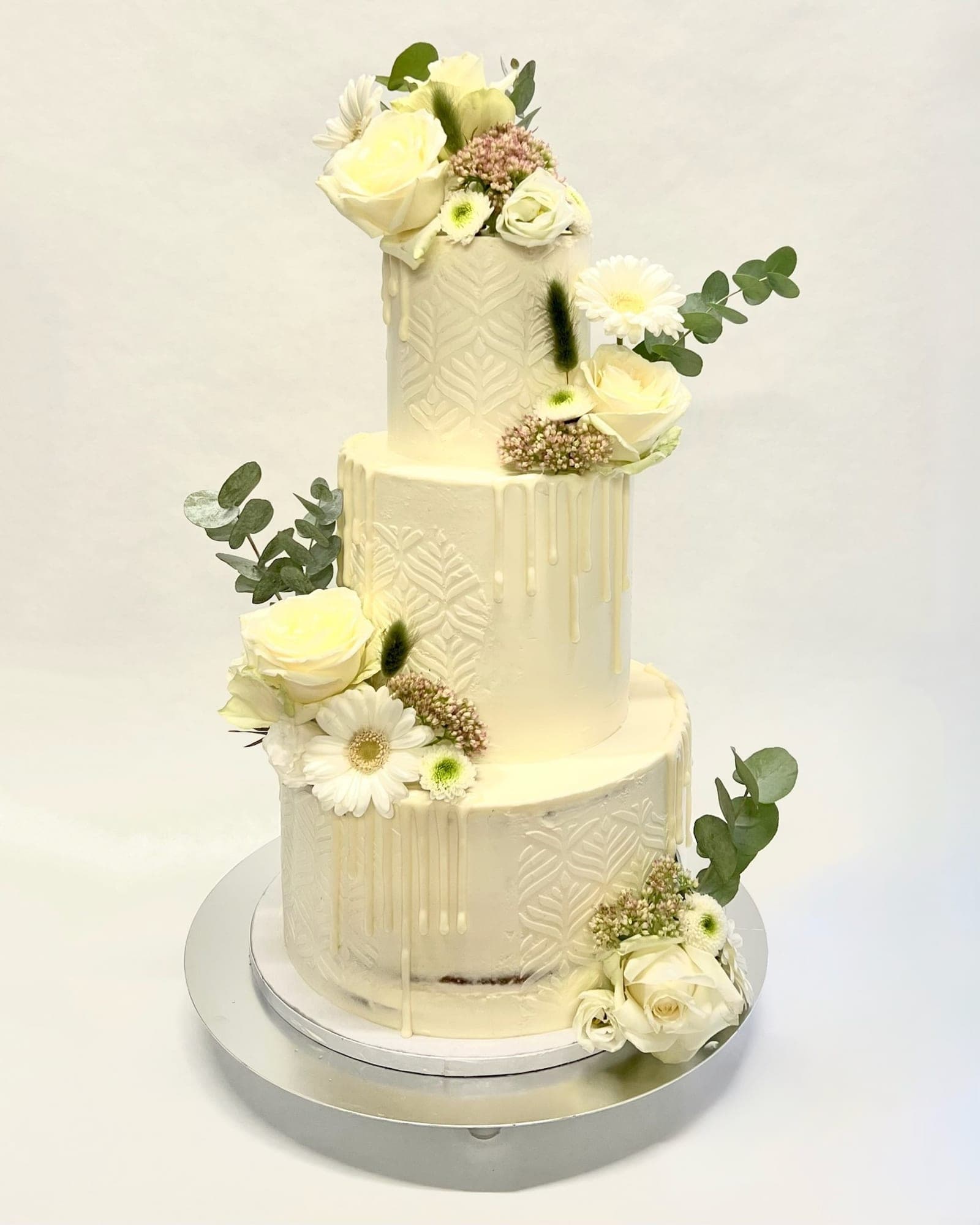 Dreistöckige Hochzeitstorte in Elfenbein mit geprägtem Muster, weißen Rosen und Eukalyptus